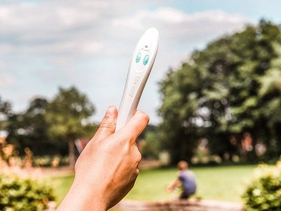 Eine Hand hält ein Bite-Away-Gerät im Freien in einem Park mit Bäumen und Gras.