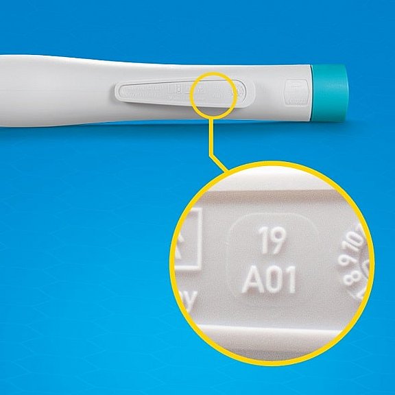 Nahaufnahme eines bite-away Stichheilers mit einem vergrößerten Ausschnitt, auf dem der Code 19 A01 eingeprägt ist. Der Griff ist weiß mit einem türkisfarbenen Ende vor blauem Hintergrund.